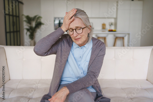 Foto Senior woman suffering from headache at home, elderly health problem, pain, stre