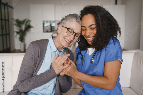 Foto Smiling nurse holding hands of senior woman on sofa at home, elderly support, he