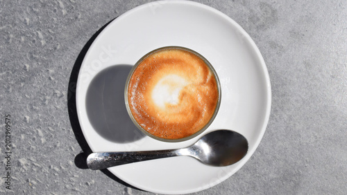 Top view of cappuccino on a white plate with a silver spoon.