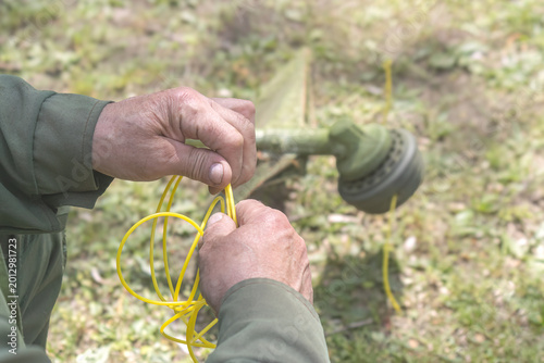 Photos Close-up of worker hands replacing yellow nylon line in grass trimmer head