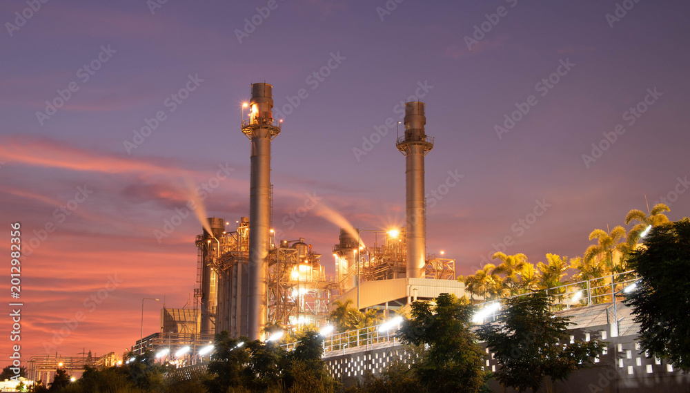 Fototapeta premium Modern power plant with chimney smokestacks and green environment against blue sky.Eco-friendly natural gas power plant surrounded by green trees and tropical garden.