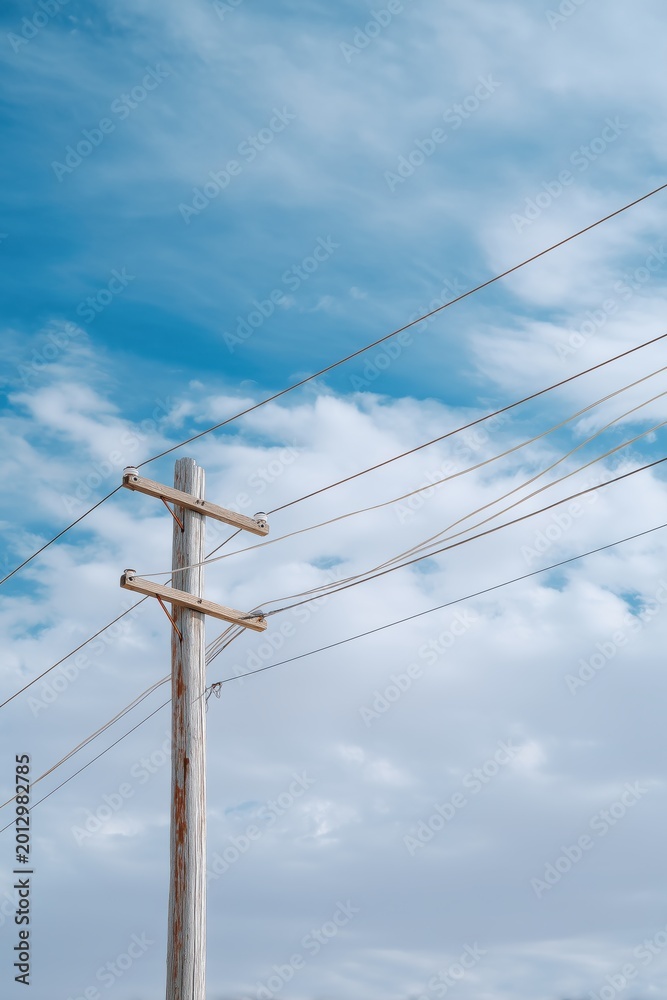 Fototapeta premium Wooden electric utility pole power lines against blue cloudy summer