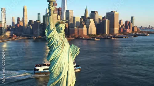 A sweeping drone video over tranquil deep blue New York Harbor, showcasing a modern ferry boat, then panning to the Manhattan skyline and majestic Statue of Liberty. Global welcome concept