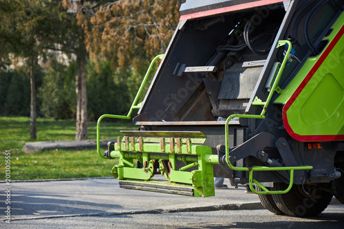 Modern green garbage truck parked on city street. Industrial vehicle for waste collection and recycling service. Professional municipal sanitization equipment for urban waste management.
