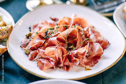 Prosciutto and cured meats on a white plate garnished with herbs and capers for appetizer