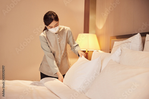 Schilderij op canvas Masked hotel housekeeper making bed in guest room
