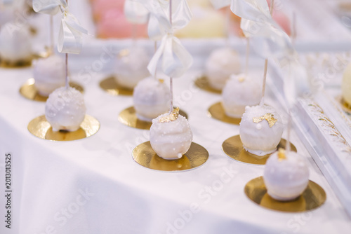 Elegant white cake pops with gold leaf and ribbons for wedding dessert table and celebration