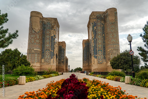 Obraz na płótnie Road leading to monumental gate ruins of Ak-Saray Palace in Shakhrisabz, surrounded by flowering shrubs and greenery