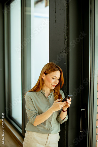 Fényképezés Woman using smartphone by window in a modern space during daytime