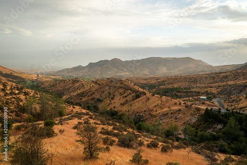 Typical autumn mountain landscape of Central Asia, featuring a winding road through foothills, colorful foliage and rugged peaks under a cloudy sky.