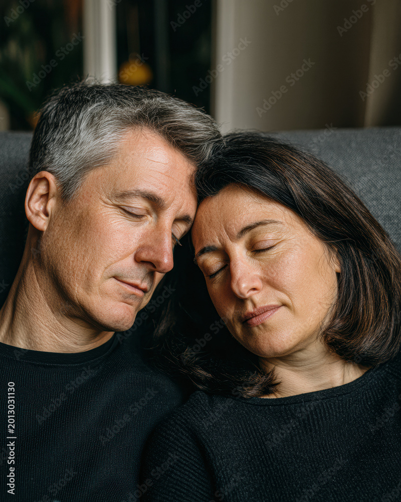 Obraz premium A middle-aged couple rests together with closed eyes, sharing a peaceful and intimate moment indoors.