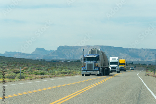 Semi-trucks haul cargo on a desert highway with mountains in background