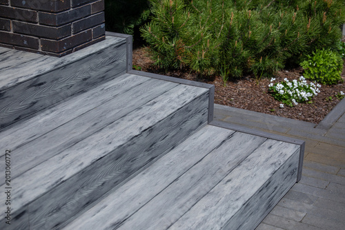 Billede på lærred Gray composite deck stairs next to dark brick column, mulched garden bed with pi