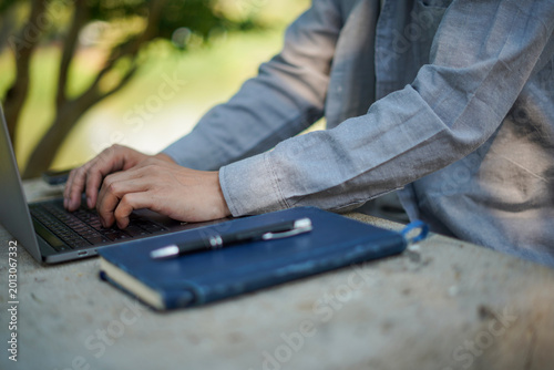 Young man sitting on the grass writing in a notebook and lying down with a book over his face, relaxing in the park. Concept of creative thinking, education, burnout, and outdoor workspace.