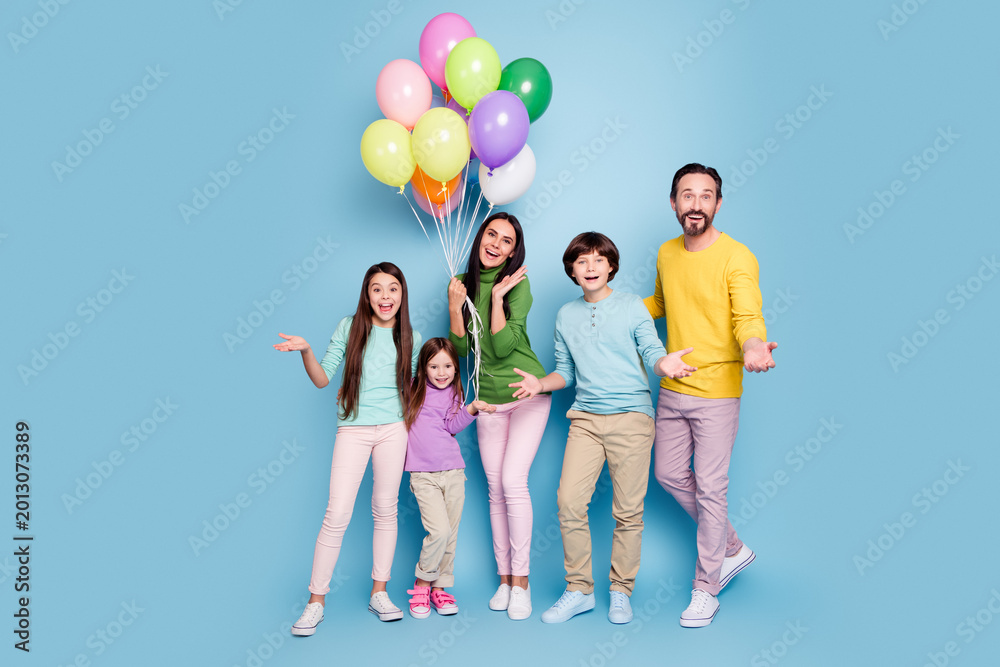 Fototapeta premium Happy family of five holding colorful balloons and smiling together against a pastel blue studio background, parents and three children in casual spring clothes celebrating a joyful moment