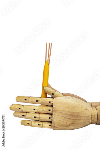 Jointed wooden mannequin hand holding a yellow beeswax candle bundled with three brown incense sticks, symbolizing Buddhist worship and religious reverence on white background