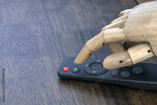Wooden Articulated Robotic Hand Pressing a TV Remote Control Button on a Dark Wooden Table, Concept of AI Automation and Smart Technology Control