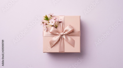 Pink gift box with elegant satin ribbon bow and cherry blossoms on purple background, Mother's Day present, spring celebration flat lay, feminine birthday gift