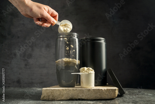 Vanilla whey protein powder and shaker, food supplements, dark background. Making protein shake drink.