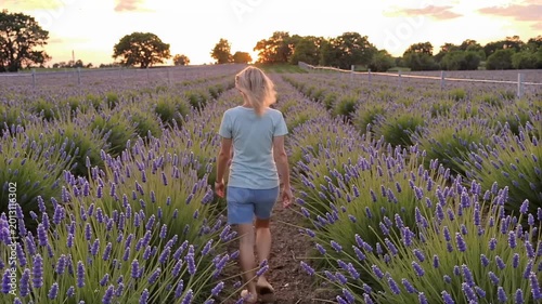 Blonde woman walking through lavender field at sunset