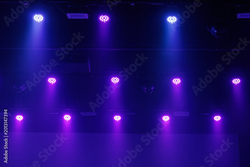 Purple and blue LED stage lights shine through haze from a dark ceiling rig, forming a moody concert background with copy space