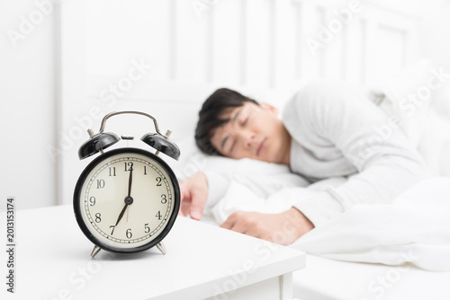 Quadro su tela Alarm Clock on Bedside Table with Sleeping Man in Bedroom