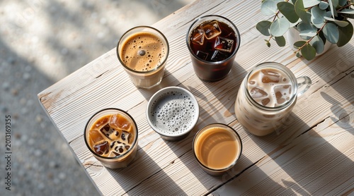 Assorted coffee drinks on wooden table. Cold brew, latte, and espresso beverages for summer refreshment. Cafe menu variety and presentation concept in bright outdoor natural light.