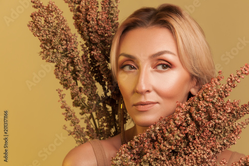 Confident blonde woman posing with autumn dried flowers looking aside posing isolated yellow studio background