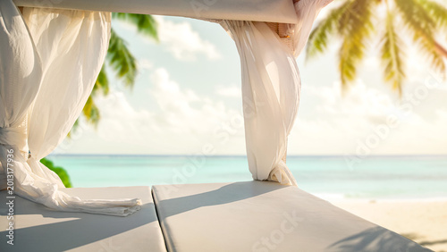 Empty floating sunbed platform on calm water on hot sunny day, featuring soft flowing canopy curtains that create airy and luxurious atmosphere. Copy space for product placement in tropic setting.
