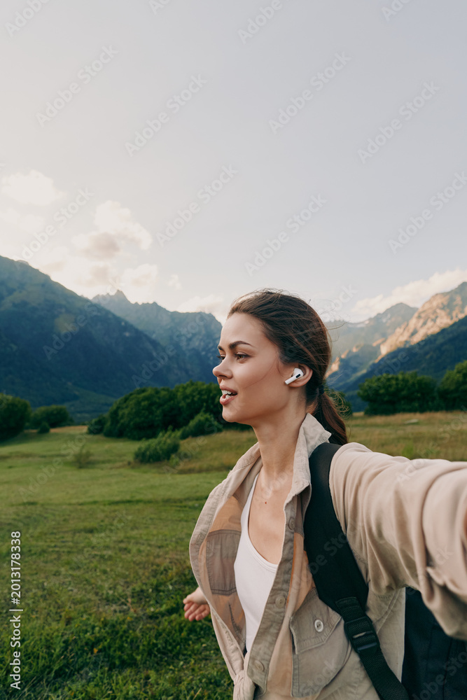 Naklejka premium A woman in a light jacket explores a green valley with mountains in the background, conveying an active outdoor lifestyle moment and scenic tranquility.