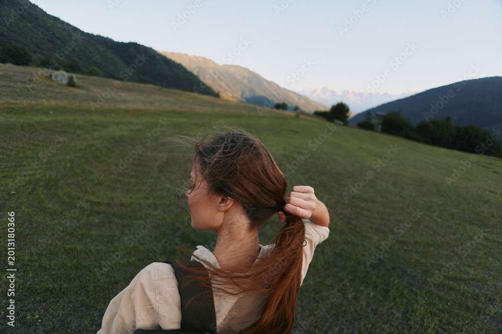 Naklejka premium Young woman outdoors in an open field ties her hair back, enjoying a peaceful moment as a gentle breeze moves across the grass.