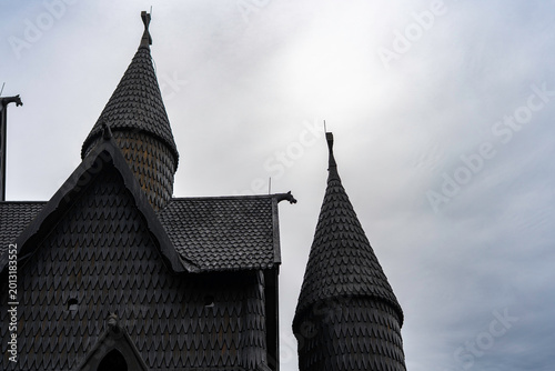 Traditional Norwegian stave church surrounded by spring countryside and forested hills under dramatic cloudy sky in Telemark, Norway. Dark wooden medieval-style architecture. 