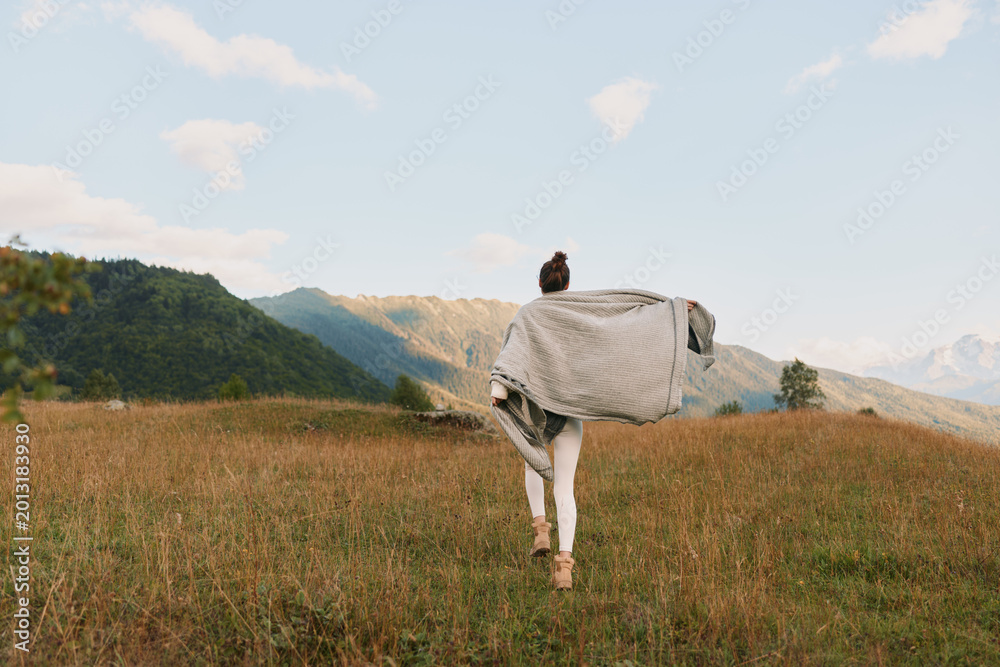 Naklejka premium Woman running through a sunlit field with a flowing shawl, open landscape, outdoor lifestyle, freedom and exploration, bright sky, distant hills, calm mood, natural light, candid moment.