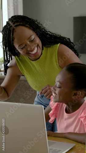 Vertical video: Leaning mother pointing at laptop, guiding daughter typing at home for homework