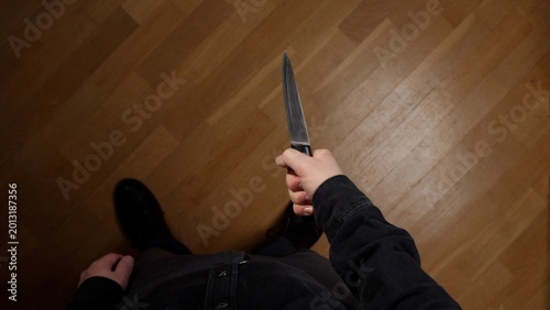 Foto Person's hand grips a sharp kitchen knife blade up over a wooden floor, overhead