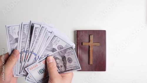 Φωτογραφία Hands fanning hundred dollar bills beside a wooden cross on a bible, top view st
