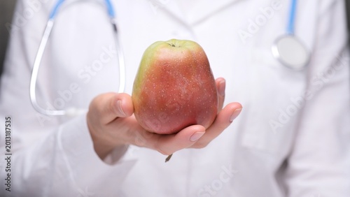 Tableau sur toile Doctor in white coat holding a fresh red and green pear, offering a symbol of he