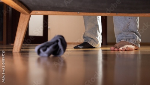 Schilderij op canvas Person in jeans standing on polished wood floor wearing one sock, bending to loo