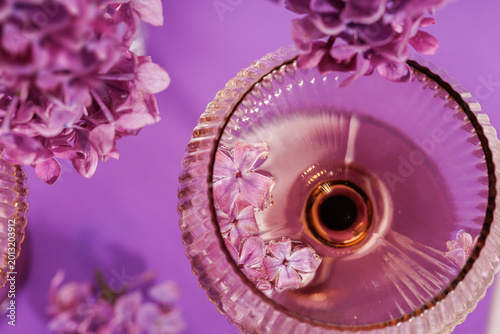 Flat lay of vintage champagne glasses with lilac blossoms and floral arrangement on a vibrant purple backdrop