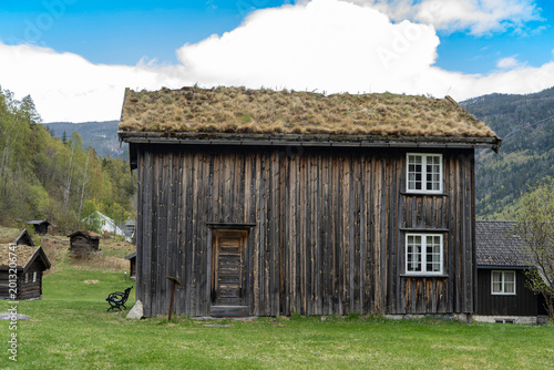 Authentic old traditional Norwegian stabbur (raised wooden storehouse) in the rural landscape of Rjukan, Telemark, Norway. Historic dark timber architecture with grass meadow, mountain forest.