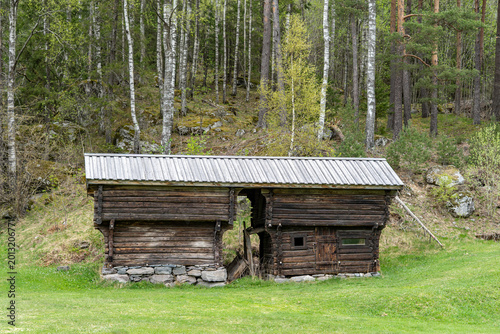 Authentic old traditional Norwegian stabbur (raised wooden storehouse) in the rural landscape of Rjukan, Telemark, Norway. Historic dark timber architecture with grass meadow, mountain forest.