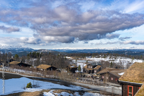  Amazing view of Norwegian mountains. Stunning landscape with traditional wooden houses and snowing tops on the horizon.