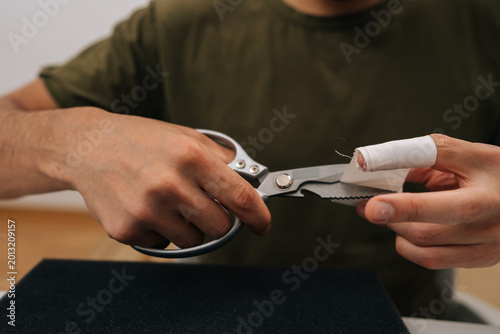 Foto Person cutting adhesive medical bandage with scissors, applying first aid to injured finger, caring for wound or minor injury, self-treatment at home or office, close-up cropped shot
