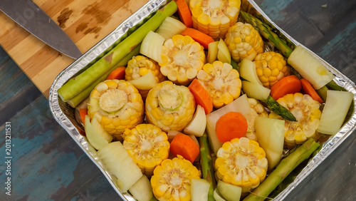 Fotografie Freshly prepared corn, carrots, and asparagus arranged in a foil tray on a rusti