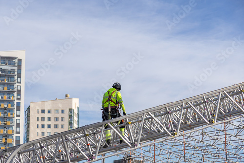 A construction worker wearing high-visibility gear and a safety harness walks carefully along a large metal truss structure during the Meritie road construction project in Espoo, Finland