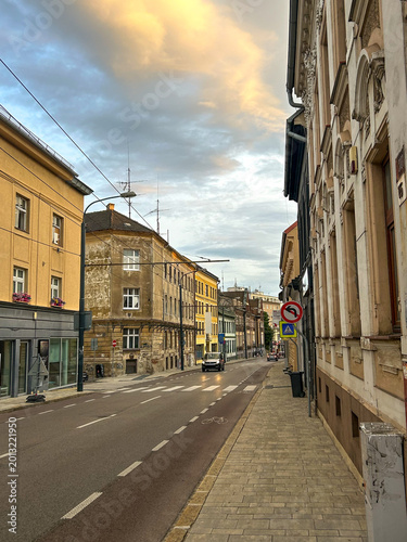Photography Quiet street in Bratislava, Slovakia with historic weathered buildings, modern apartment tower, tram wires, and dramatic evening clouds creating a contrasting urban atmosphere