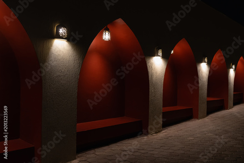 Atmospheric night view of traditional Arabic arched niches with warm lantern lighting on red textured walls for luxury travel concept