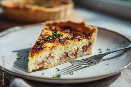 Slice of quiche Lorraine with bacon on a white plate and fork