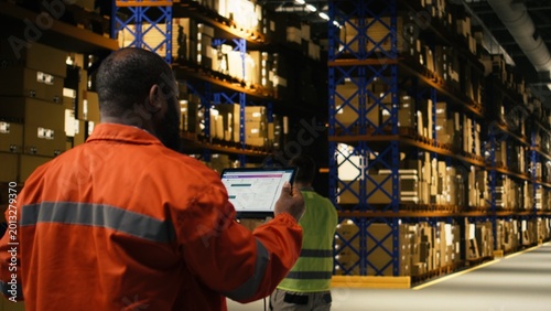 Tableau sur toile Black worker verifying cargo with tablet and scanner for shipment in depot