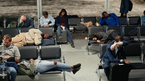 Tableau sur toile Fatigued people in airport lounge lying down on metallic benches during prolonged layover